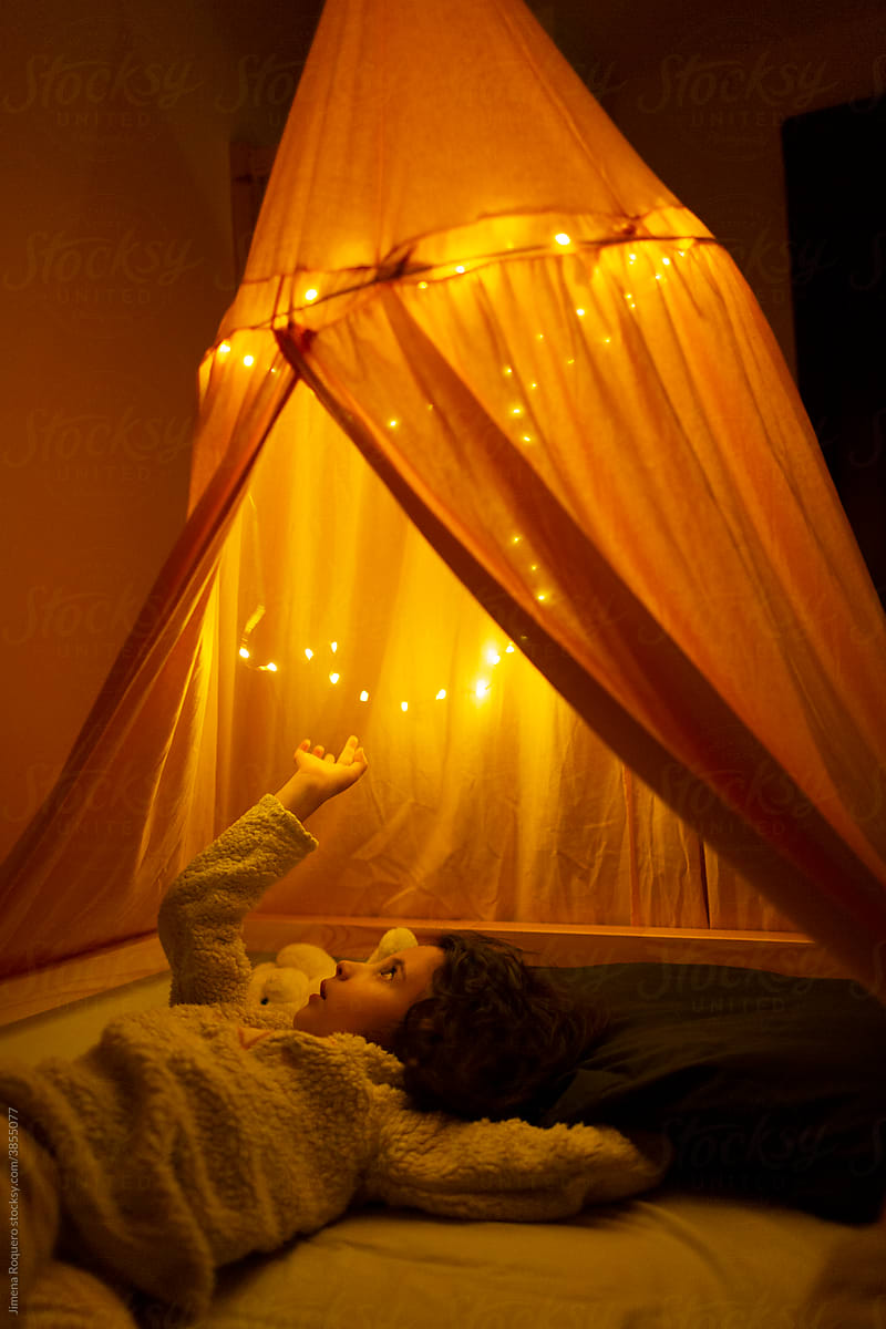 Kid Lying On Bed Under Tent With Fairy Lights by Stocksy