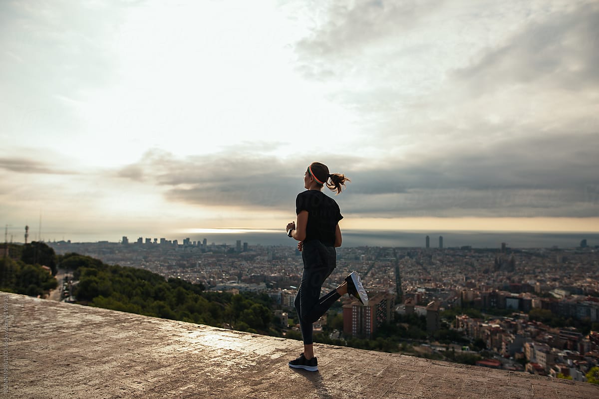 Fit woman running above city at sunrise.