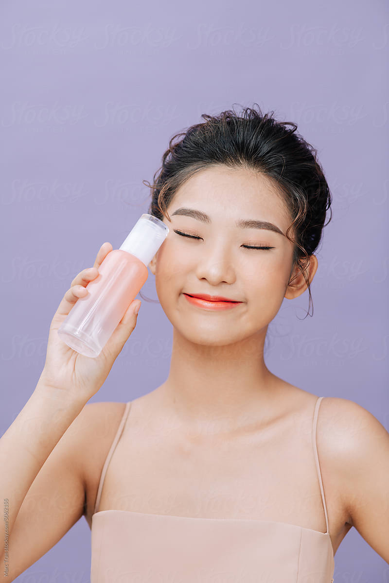Pretty Asian young woman posing with cosmetic bottle