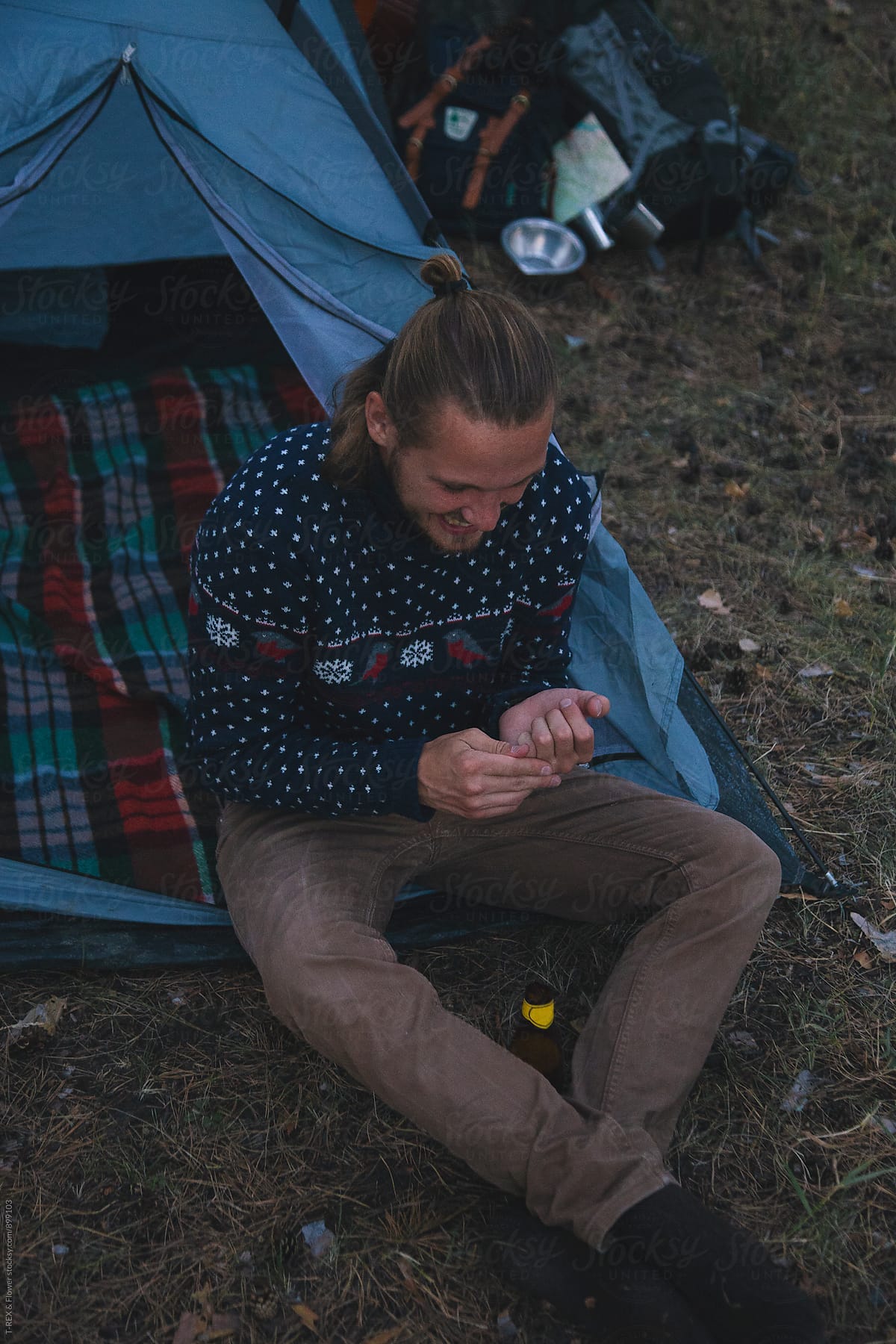 Young blond man in sweater sitting near tent