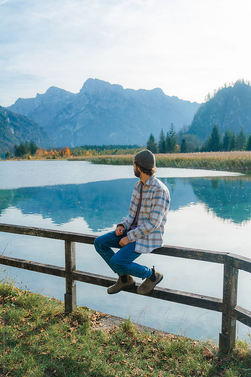 Man sitting on fence on the background of alpine lake enjoying view