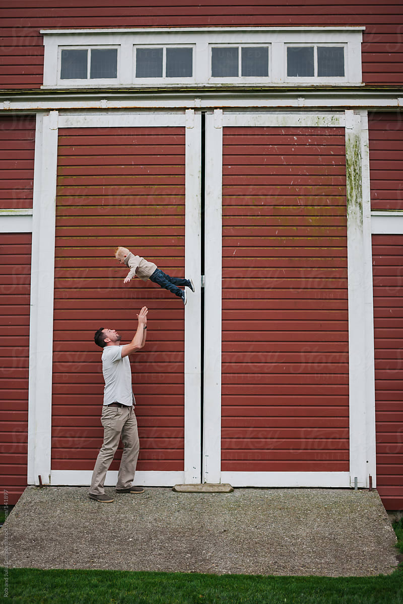Dad throwing young son up in the air in front of farm barn door