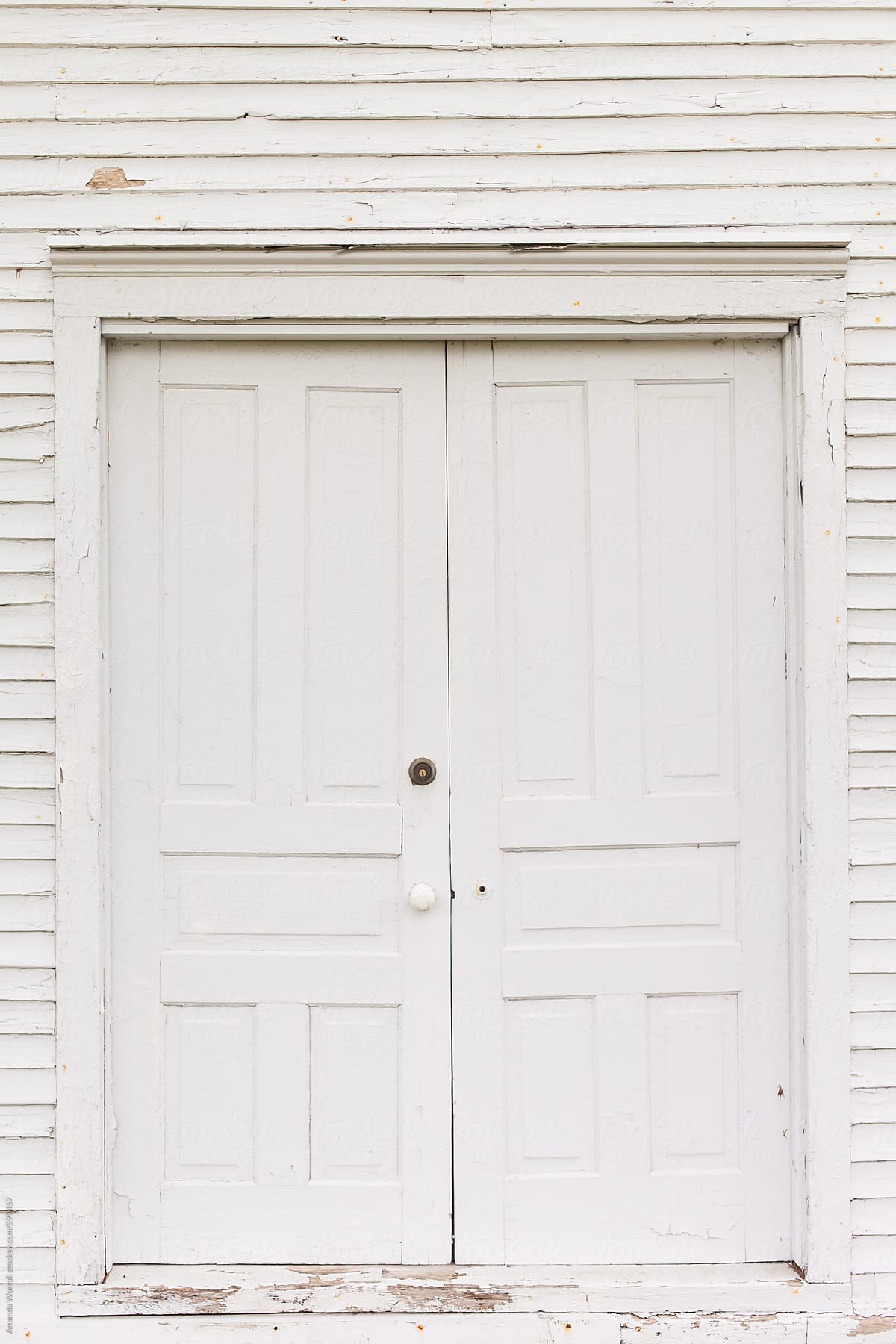 Old white paneled double doors with white siding