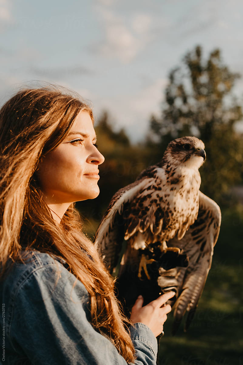 A woman in her twenties posing for a portrait with an owl in a forest