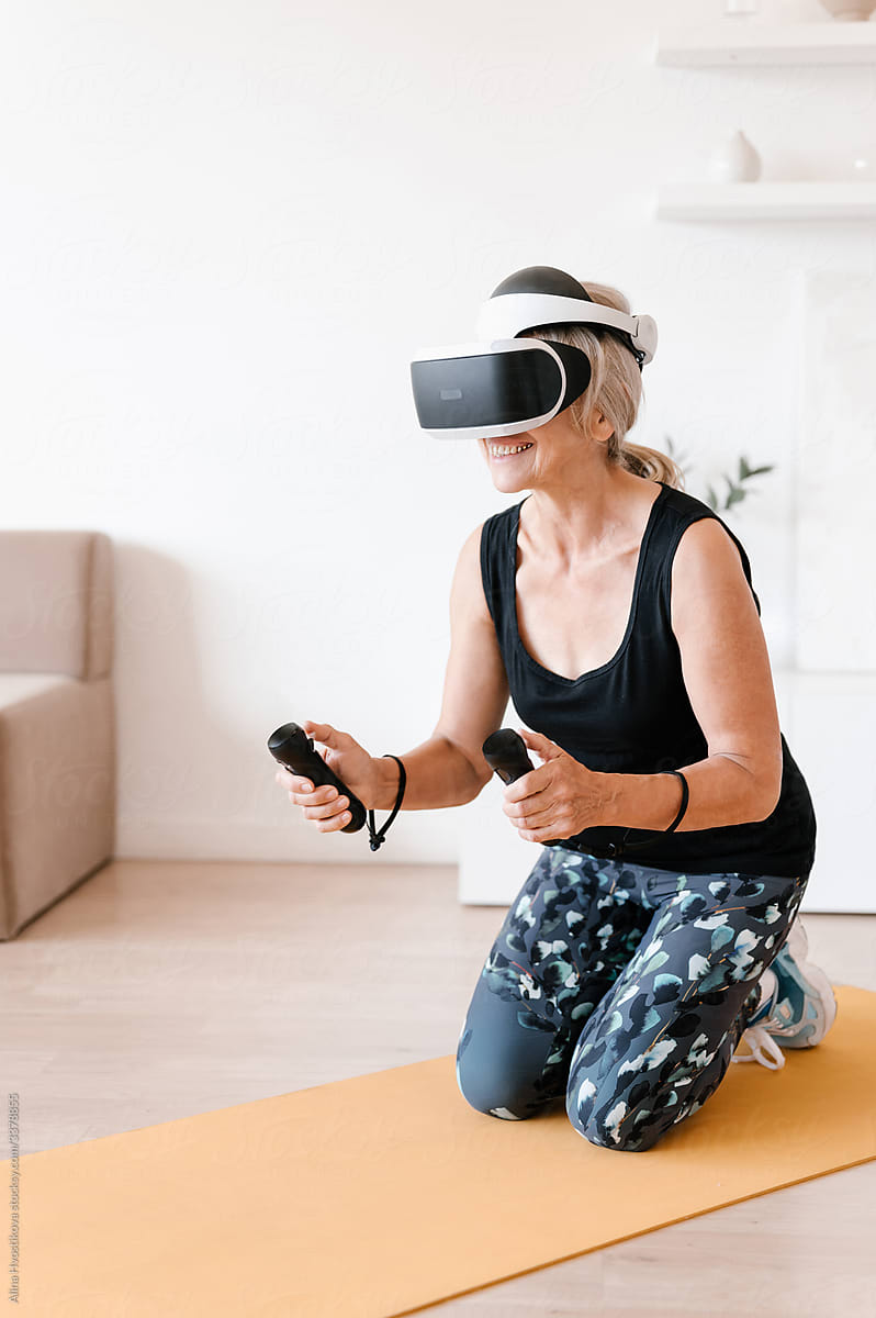 Elderly sportswoman in VR goggles exercising on mat