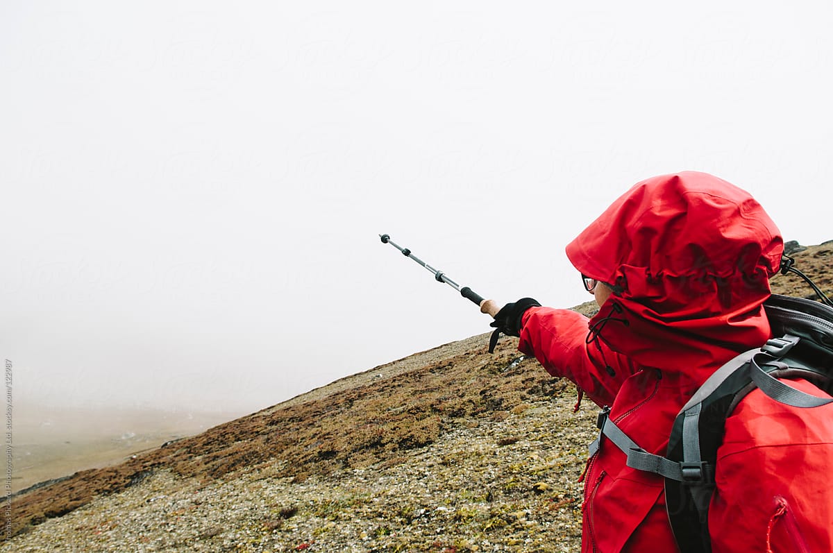 Female trekker pointing with a trekking pole to mountains obscured by cloud, Everest Region, Nepal.