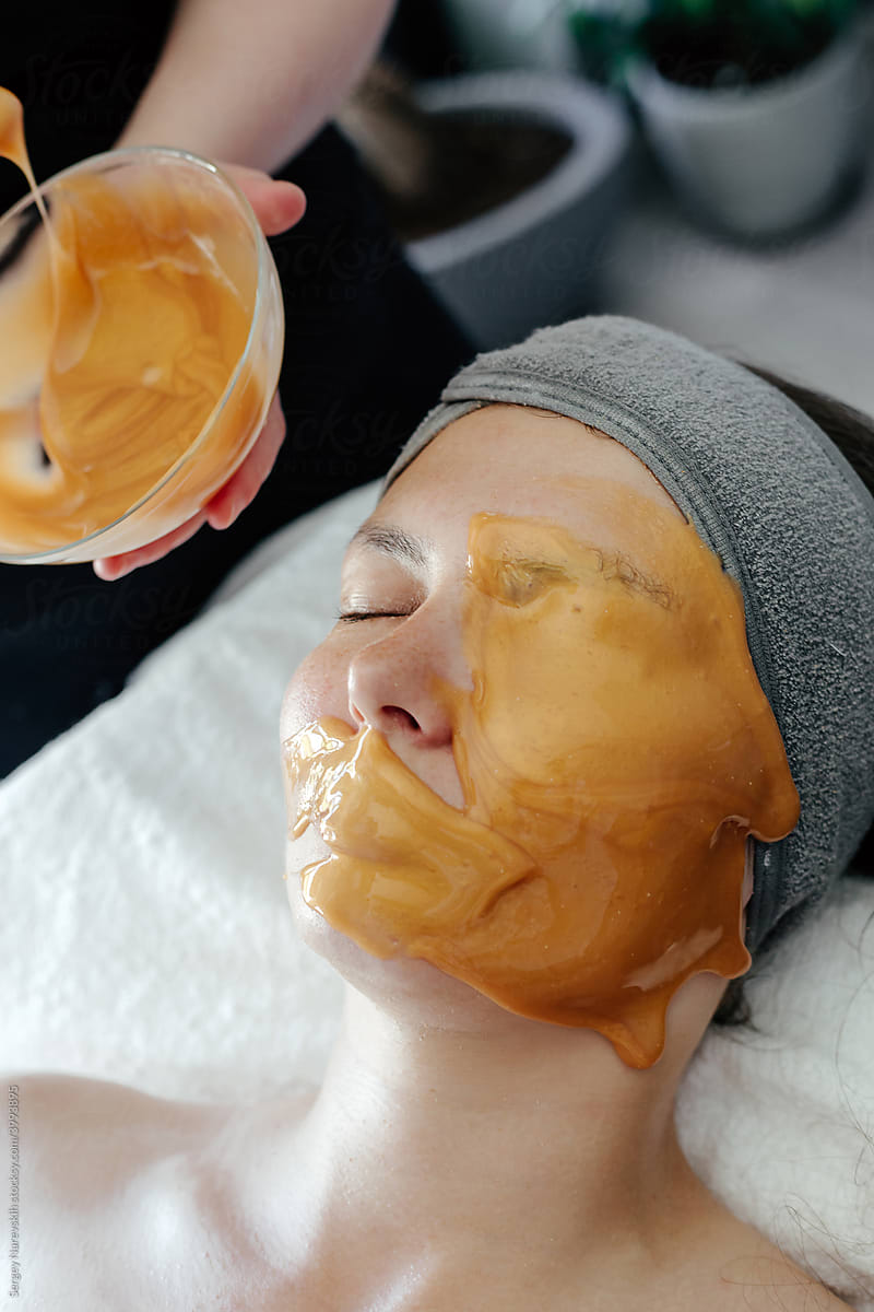 Crop cosmetician applying mask on face of woman