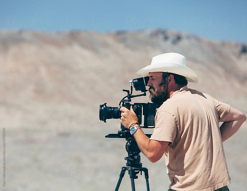 Filmmaker using digital cinema camera, composing shot, desert in distance