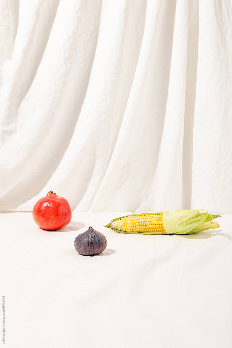 Corn, fig, and pomegranate on the white linen material.