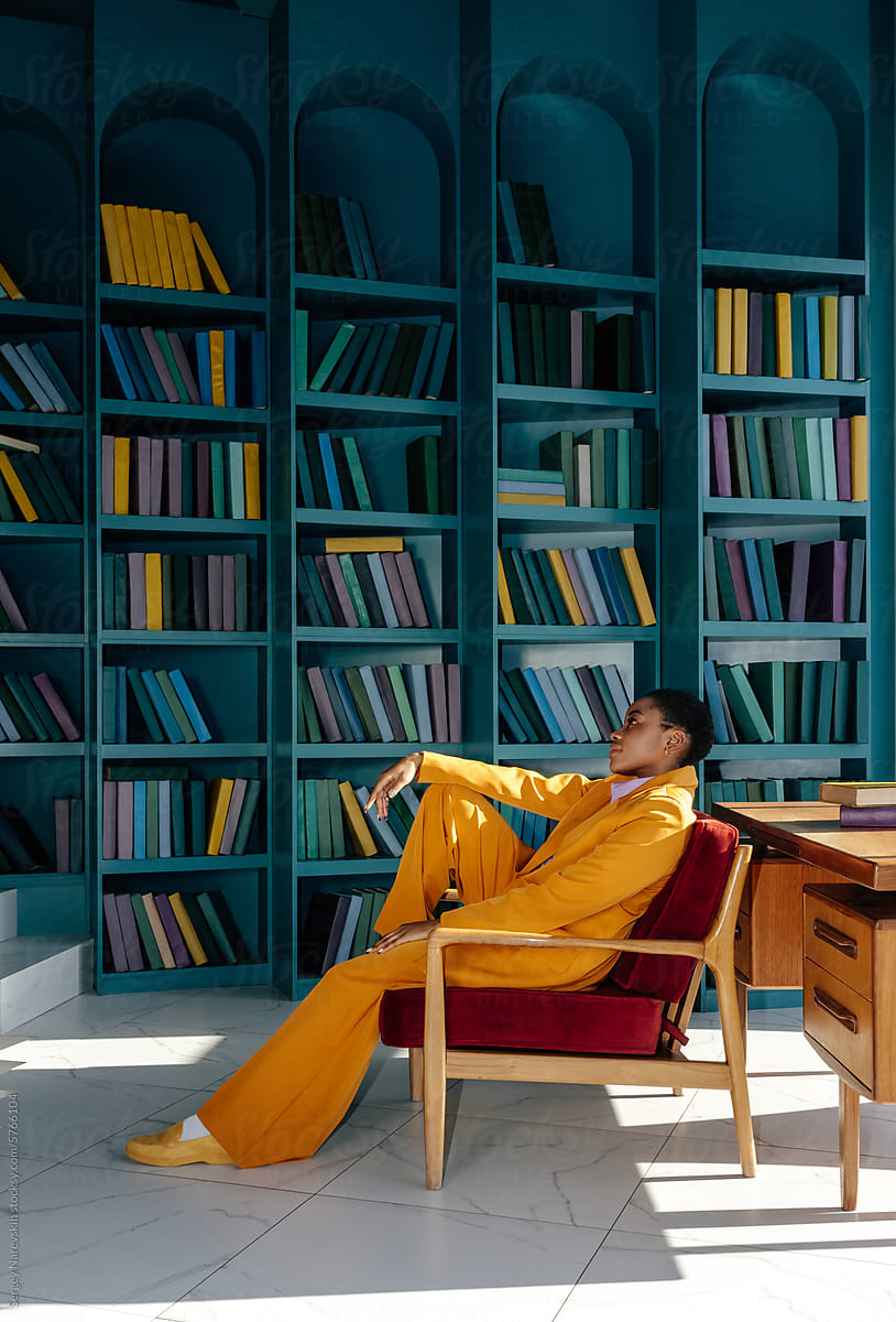 Dreamy woman in yellow suit sitting in armchair in cabinet