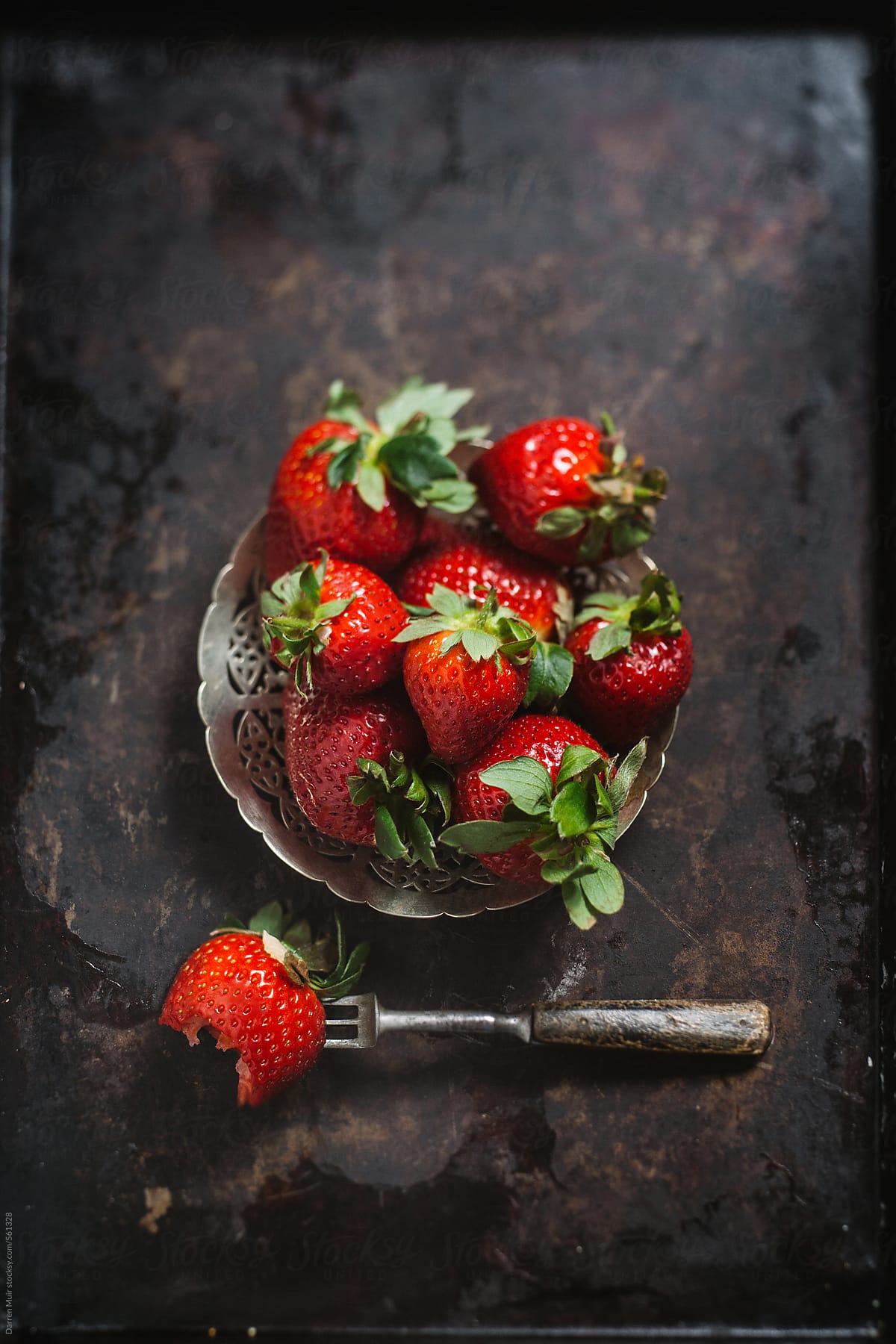 Fresh strawberry's on metal background with fork, one with a bite out of it. Seen from above.