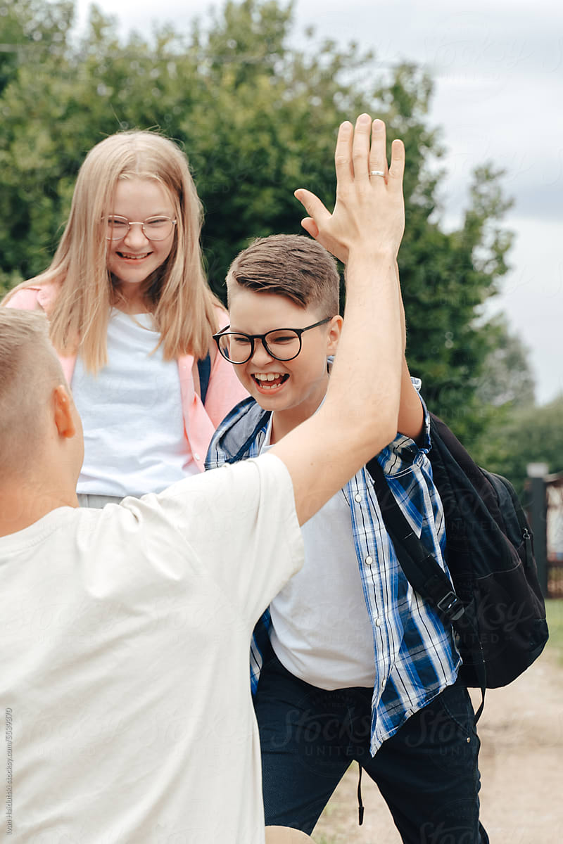 Dad giving high five to smiling teen daughter, son heading to school