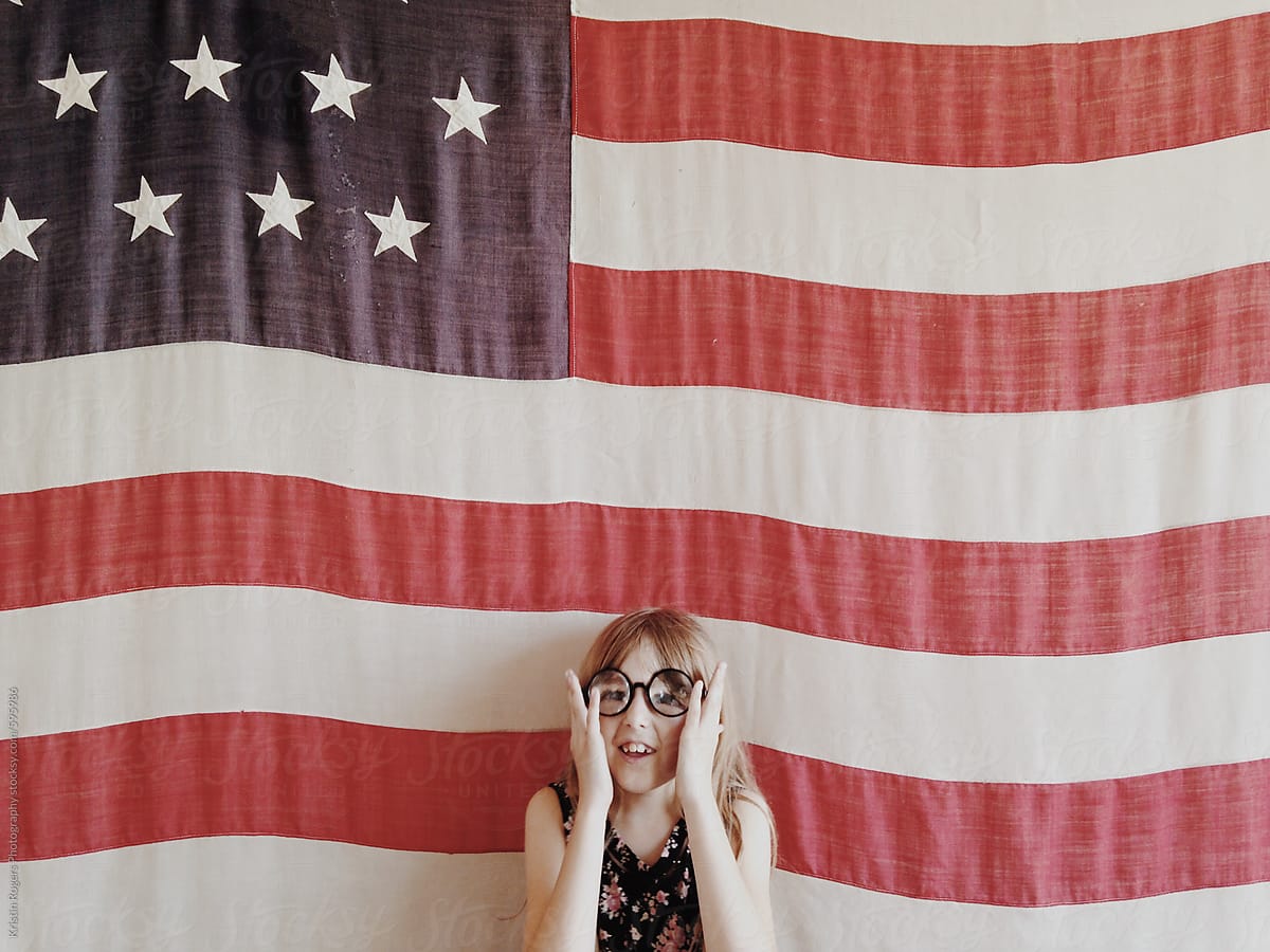 young  girl wearing silly glasses in front of flag