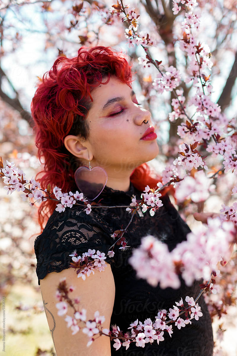 Nonbinary person posing between almond tree in blossom in profile