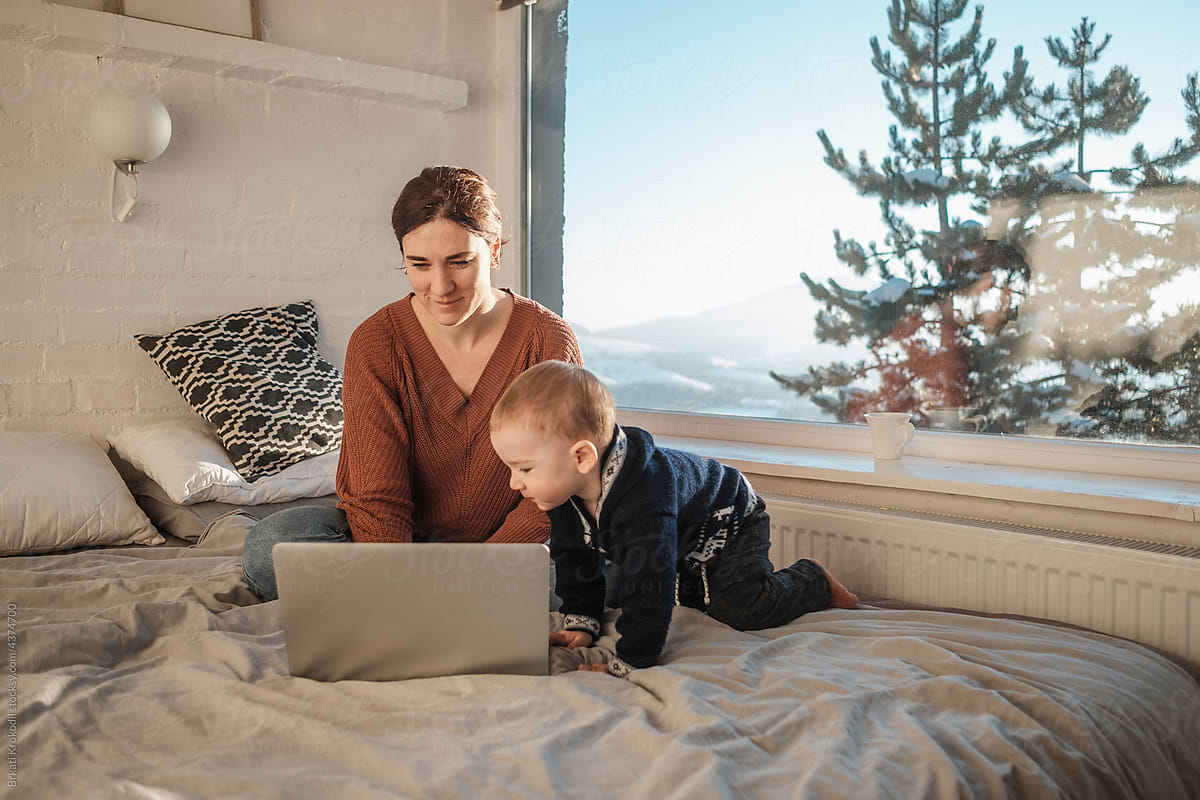 Mother And Baby Boy Sitting On The Bed With Laptop