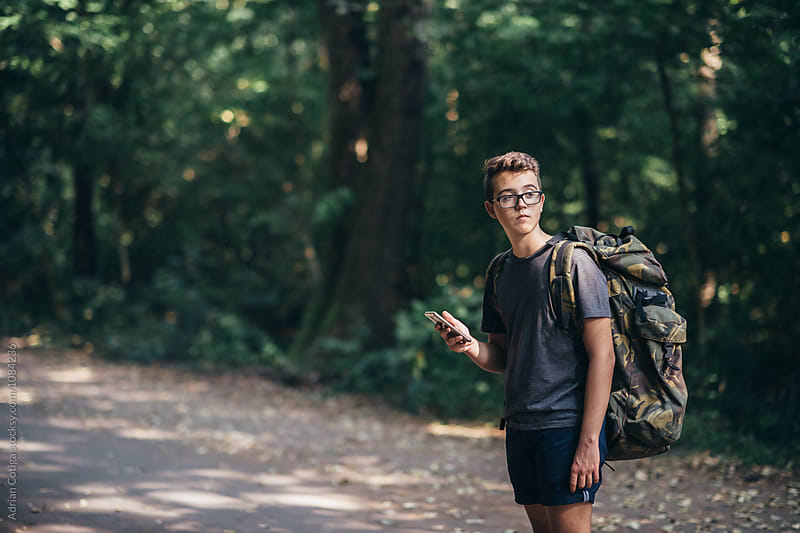 Young teen boy with a backpack exploring the forest, and using smartphone