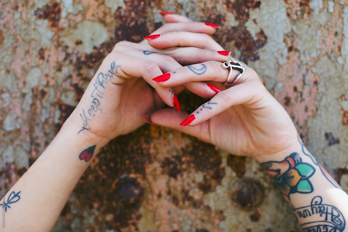 Alternative woman with tattoos and red nail polish in front a rusted wall.
