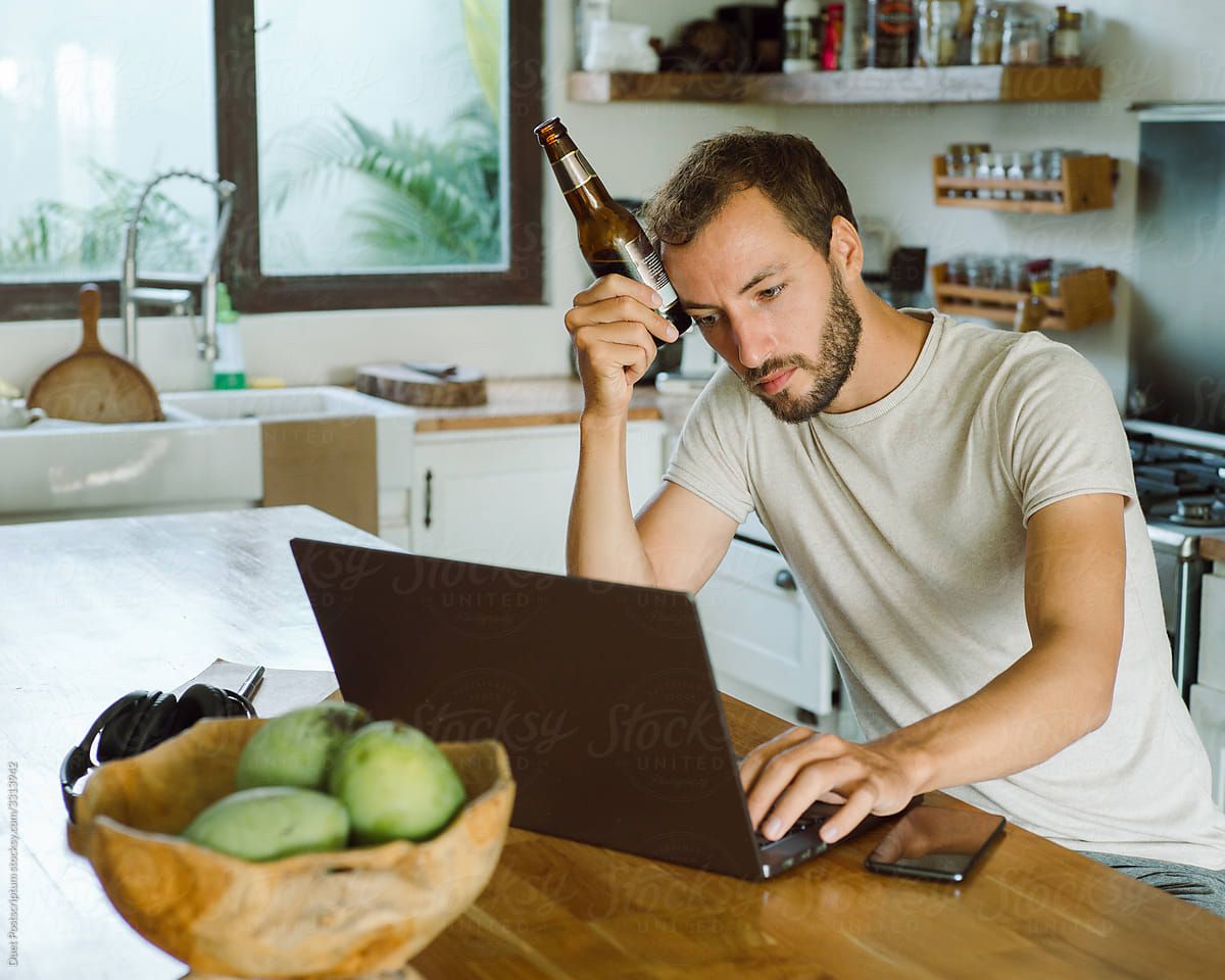 Man with beer working on laptop from home