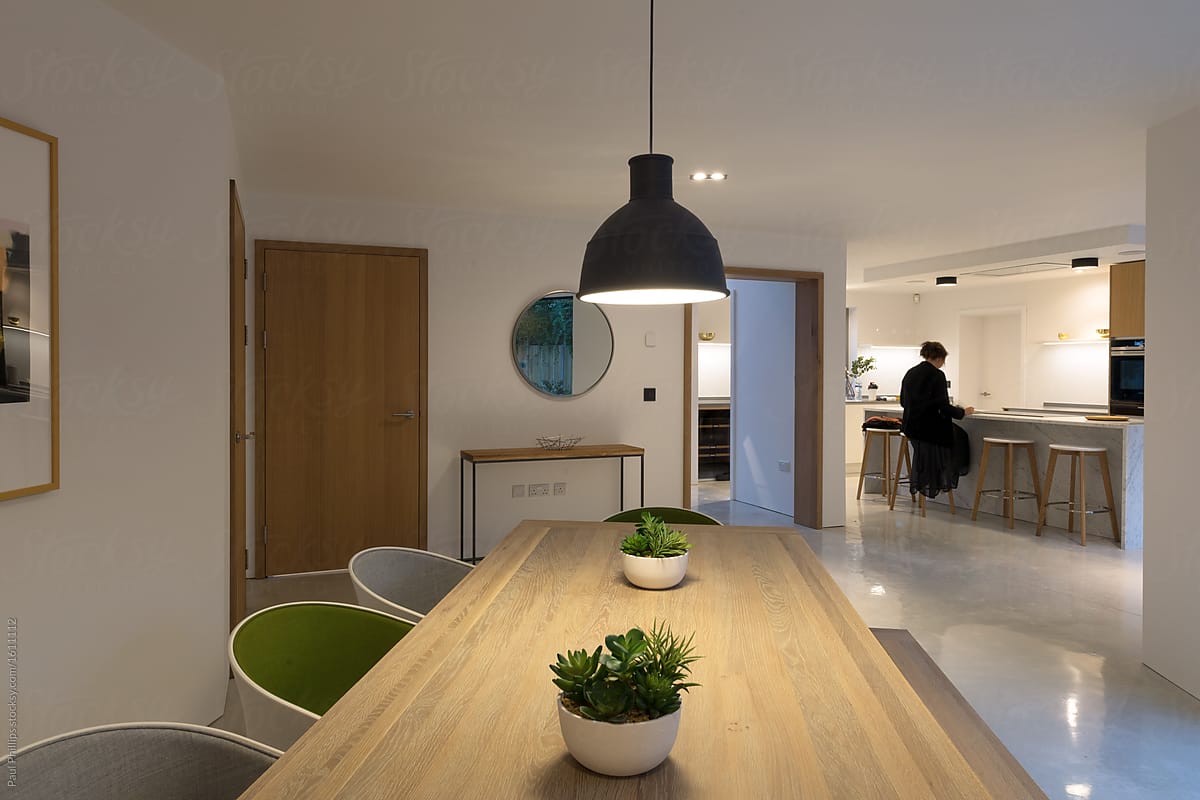 Evening picture of a modern dining and kitchen area in the evening. Woman sitting at the counter.