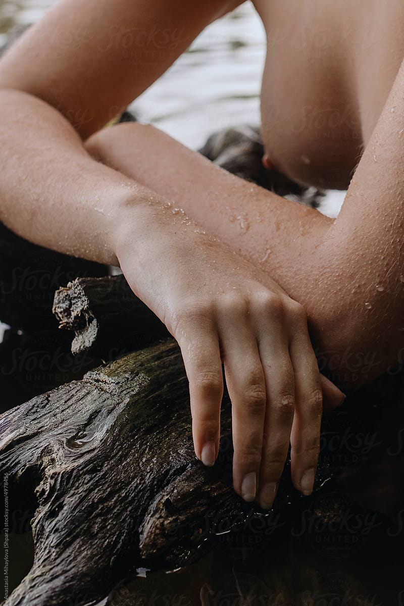 Close-up hand, breast and nipple of wet naked woman on wood in water