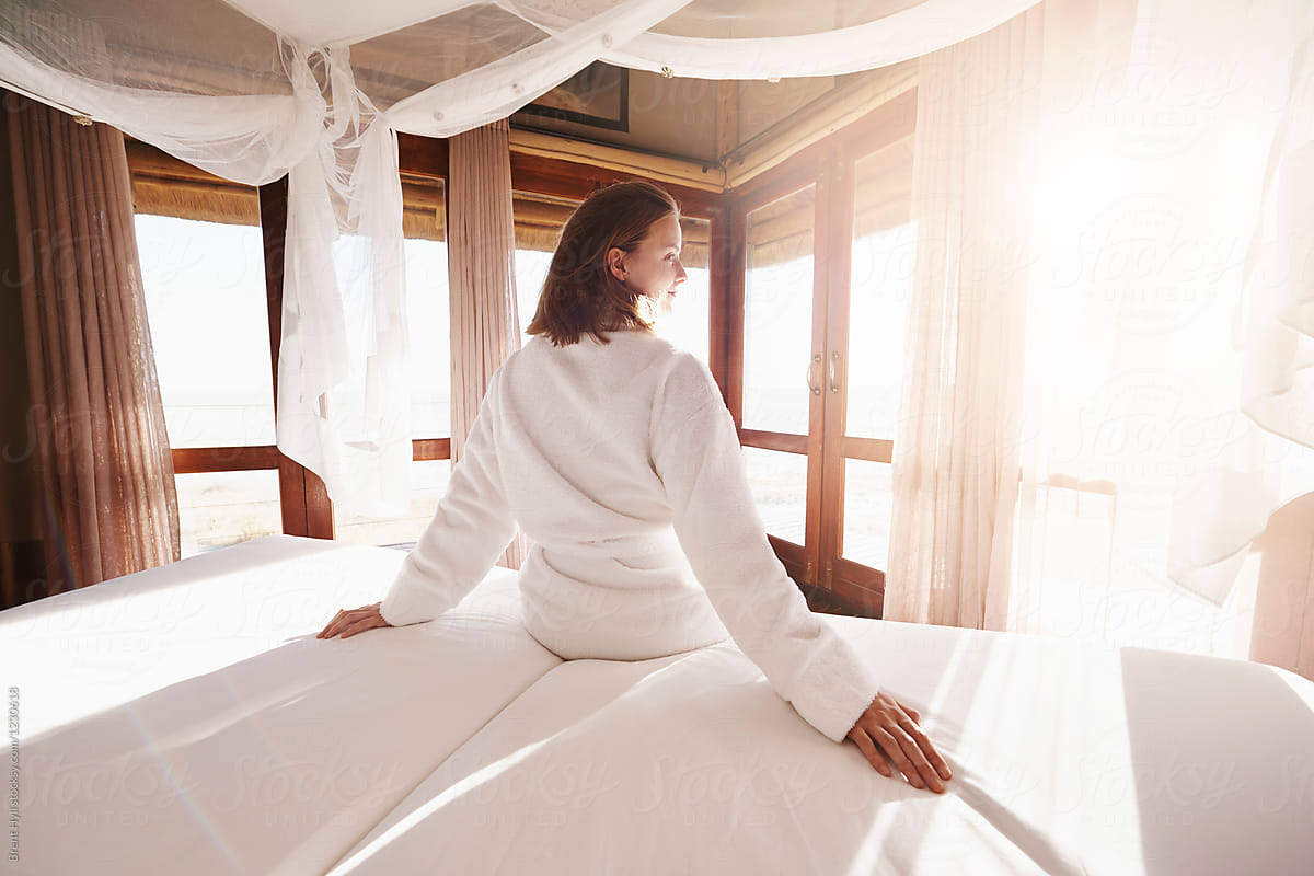 Young woman in a bathrobe watching the sunrise from her hotel bed
