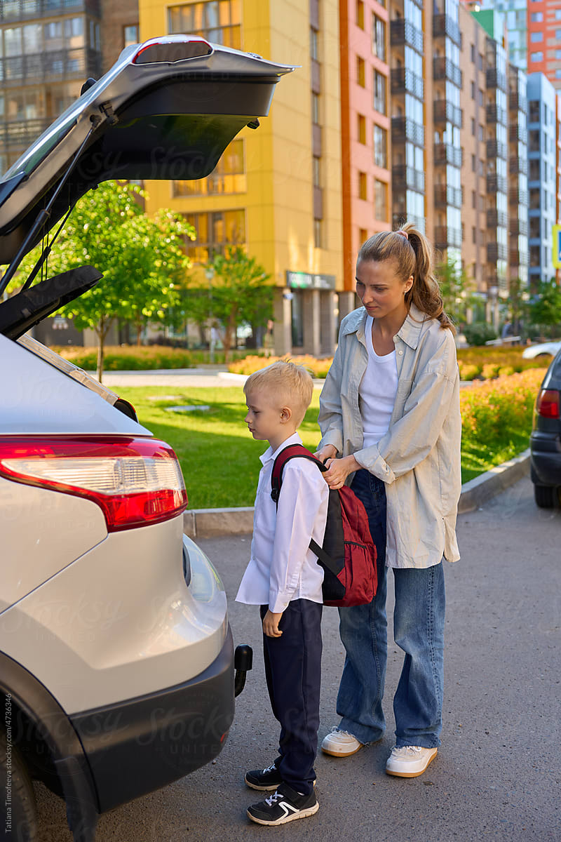mother with a schoolboy child is standing near the car with a backpa