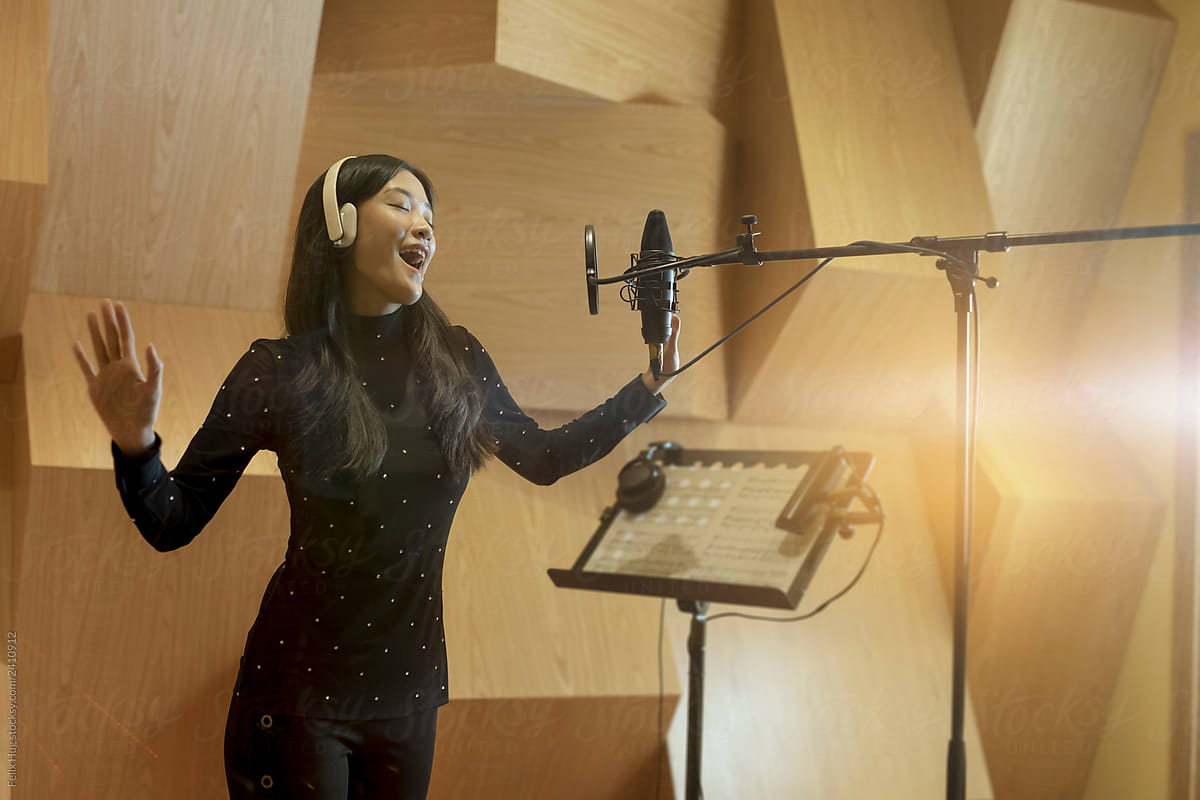 A musician is recording her vocal music in a wooden recording studio.