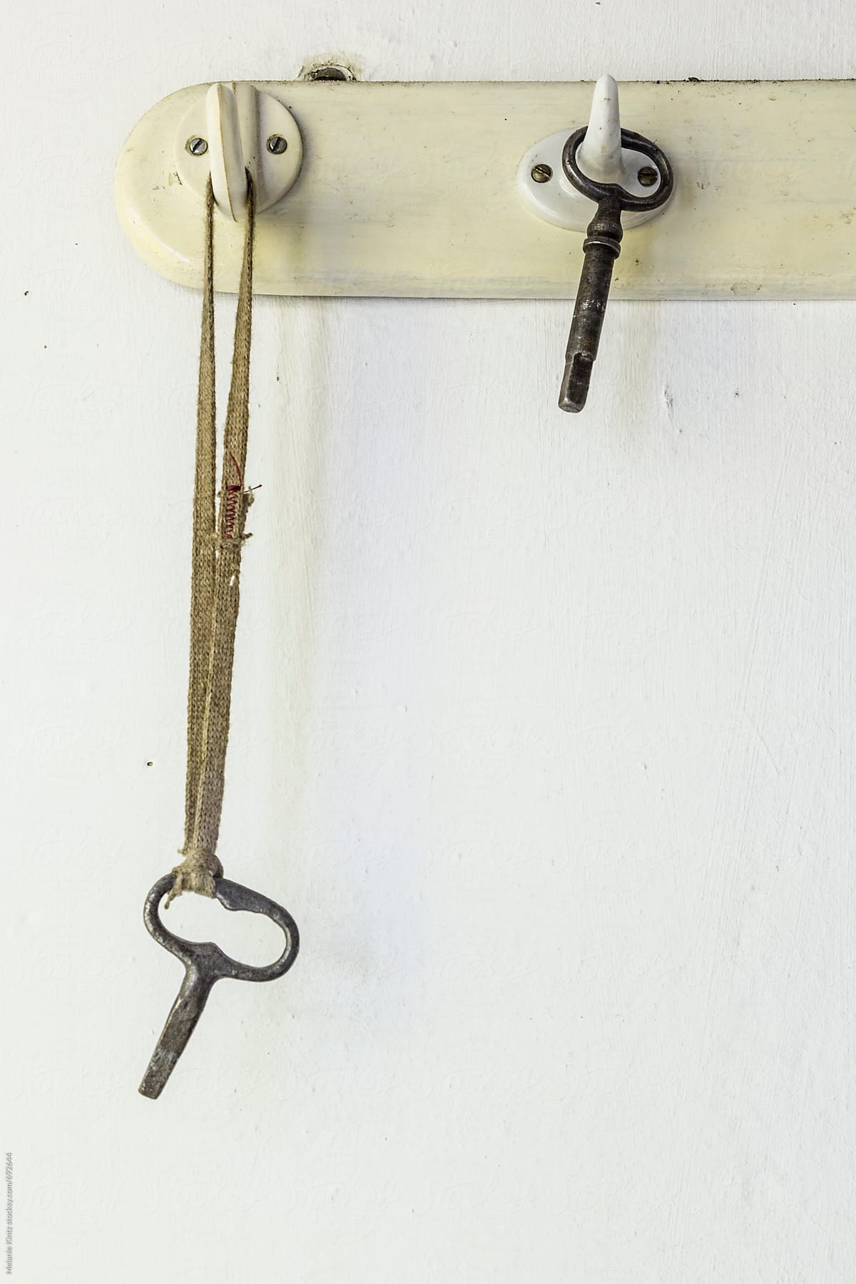 Oldfashioned keys are hanging on a board with hooks on a white wall