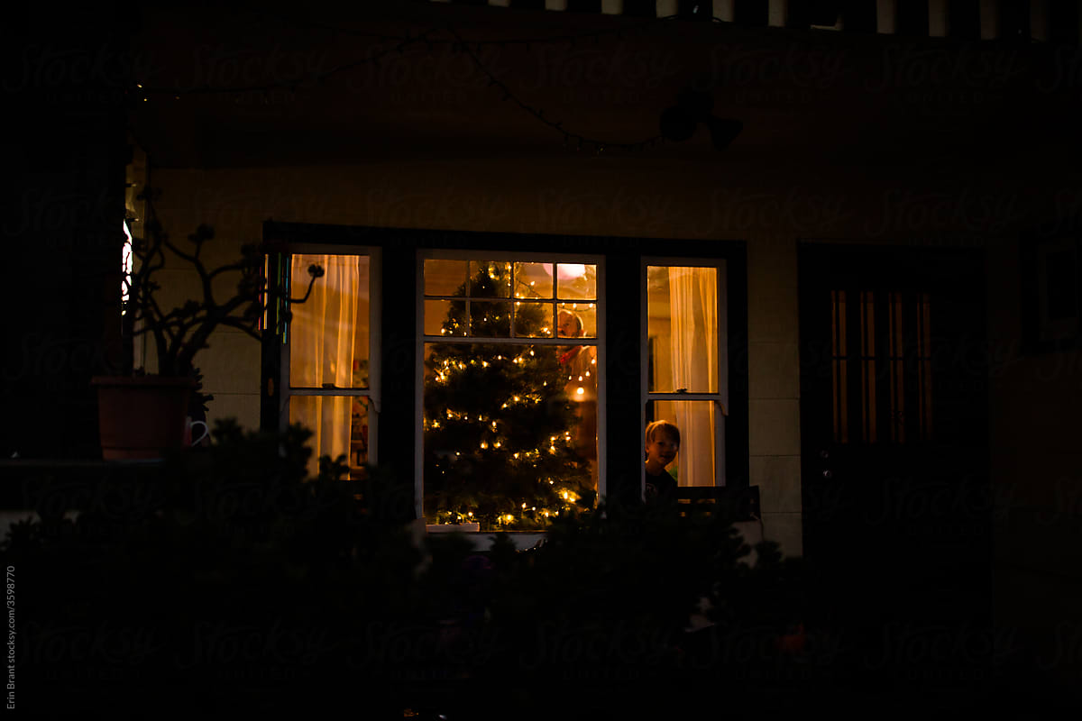Outside view of young child peering through window while father decorates tree inside