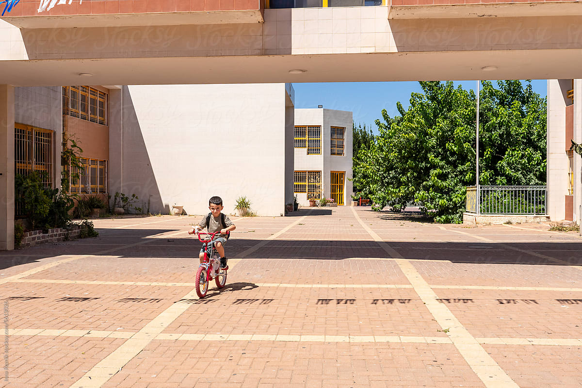Boy on a Sunny Day Rides a Bicycle Through the School Yard.