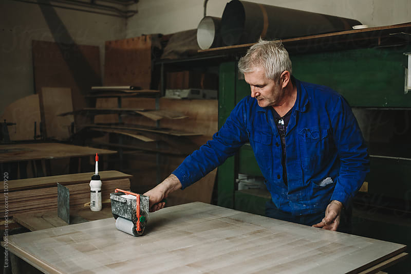 senior woodworker applying glue on wooden veneer