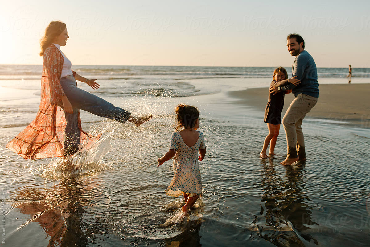 Happy family playing in ocean tide at sunset