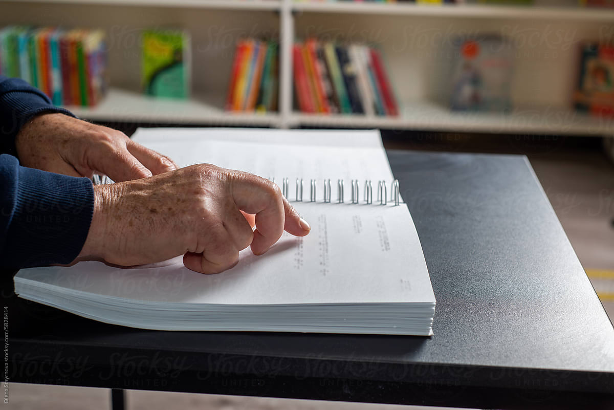 Male elderly fingers reading a book page with braille