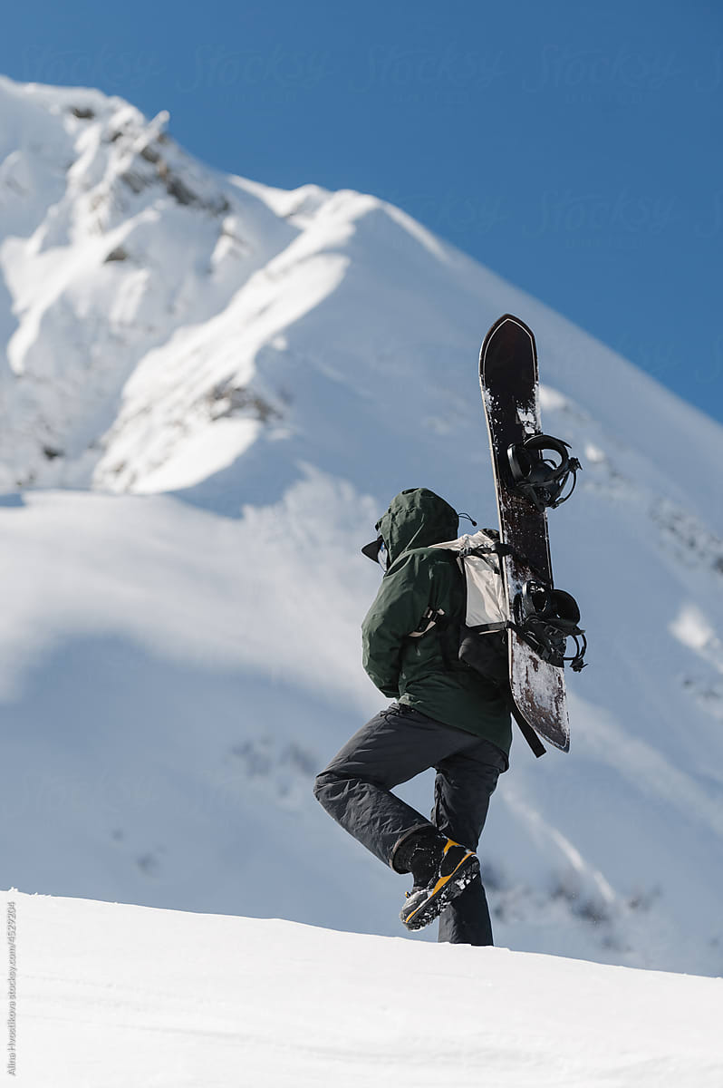 Unrecognizable snowboarder walking near snowy mountain