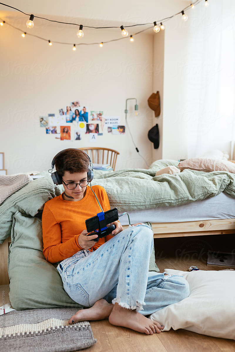 Focused teen gamer playing videogame near bed