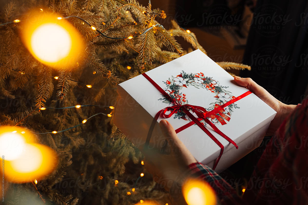 Woman Unwrapping gift box near xmas tree at home in Christmas morning