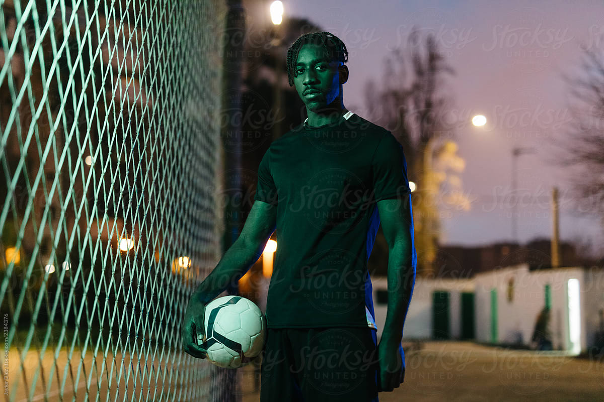 African American man holding ball near fence at night
