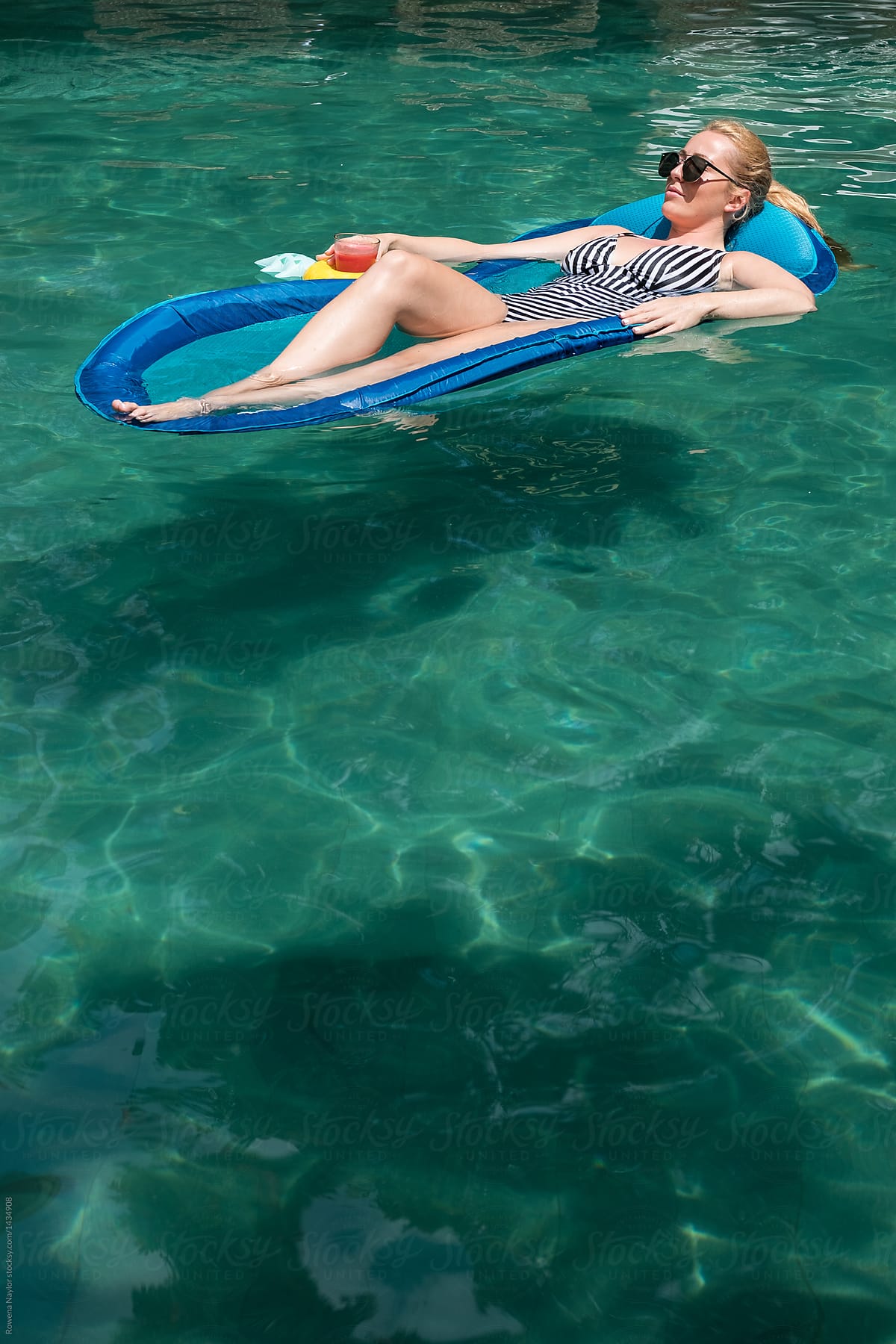 Attractive young woman sunbathing on floating bed in pool