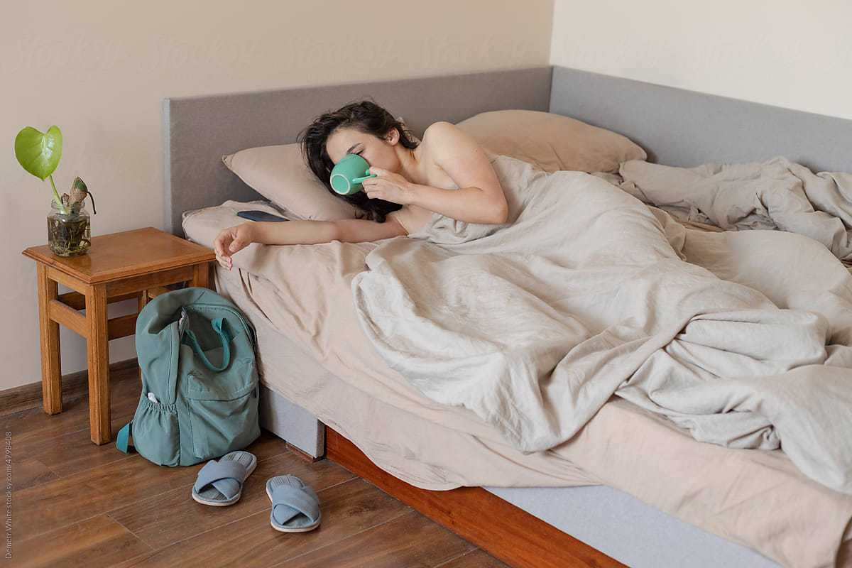 woman in bed drinking water from a mug