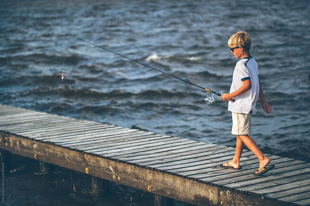 Boy Carrying His Fishing Pole Out On A Pier by Stocksy