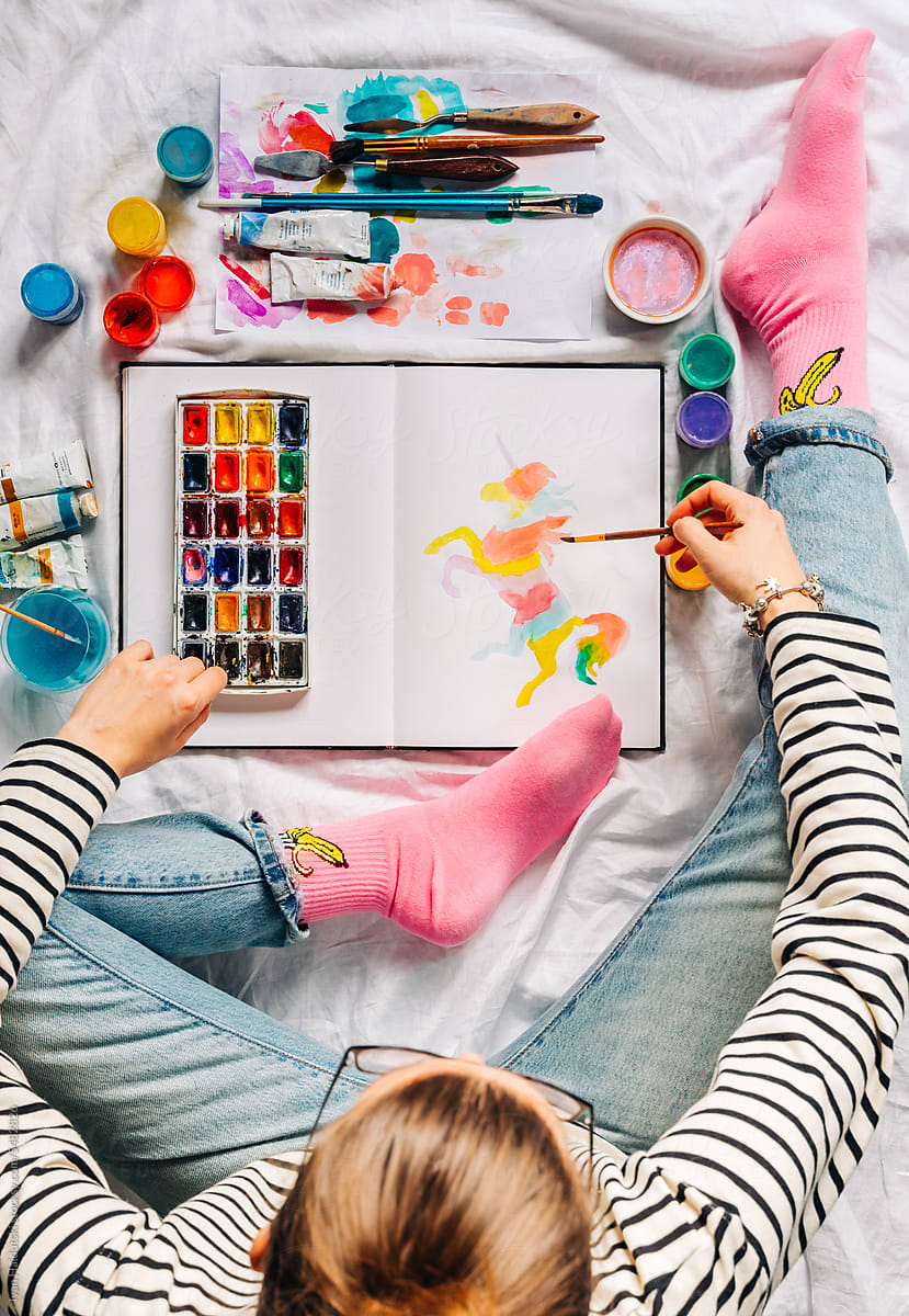 Female designer artist drawing colorful unicorn in sketchbook