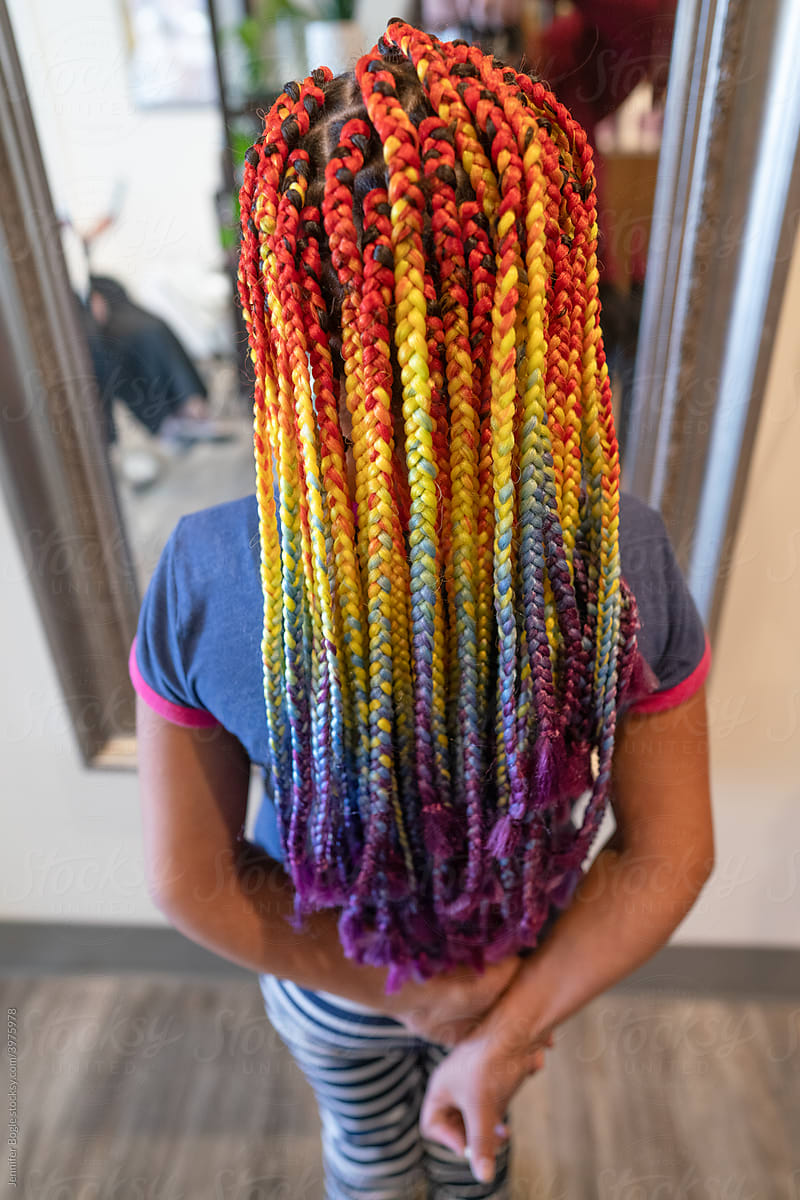 Girl with rainbow braids in front of salon mirror