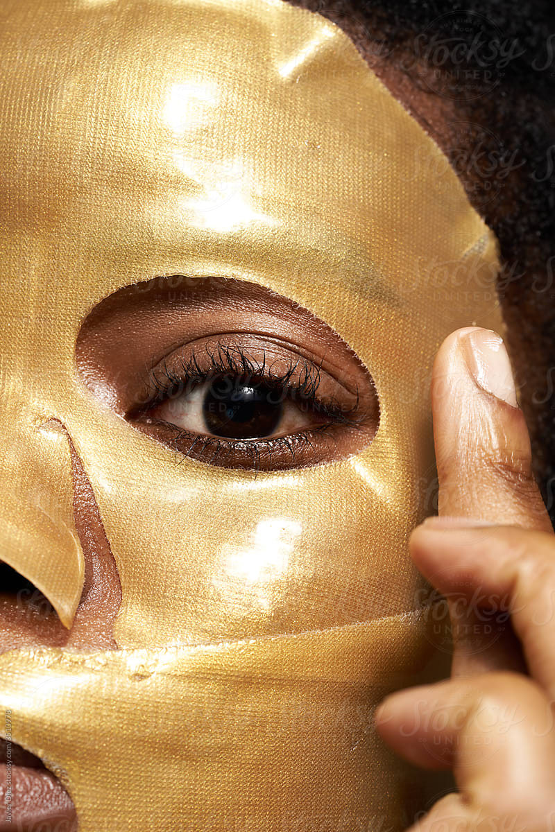 Woman applying golden cosmetic mask on face