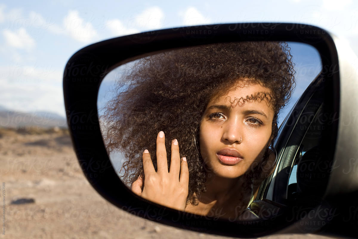 young woman looking in car mirror