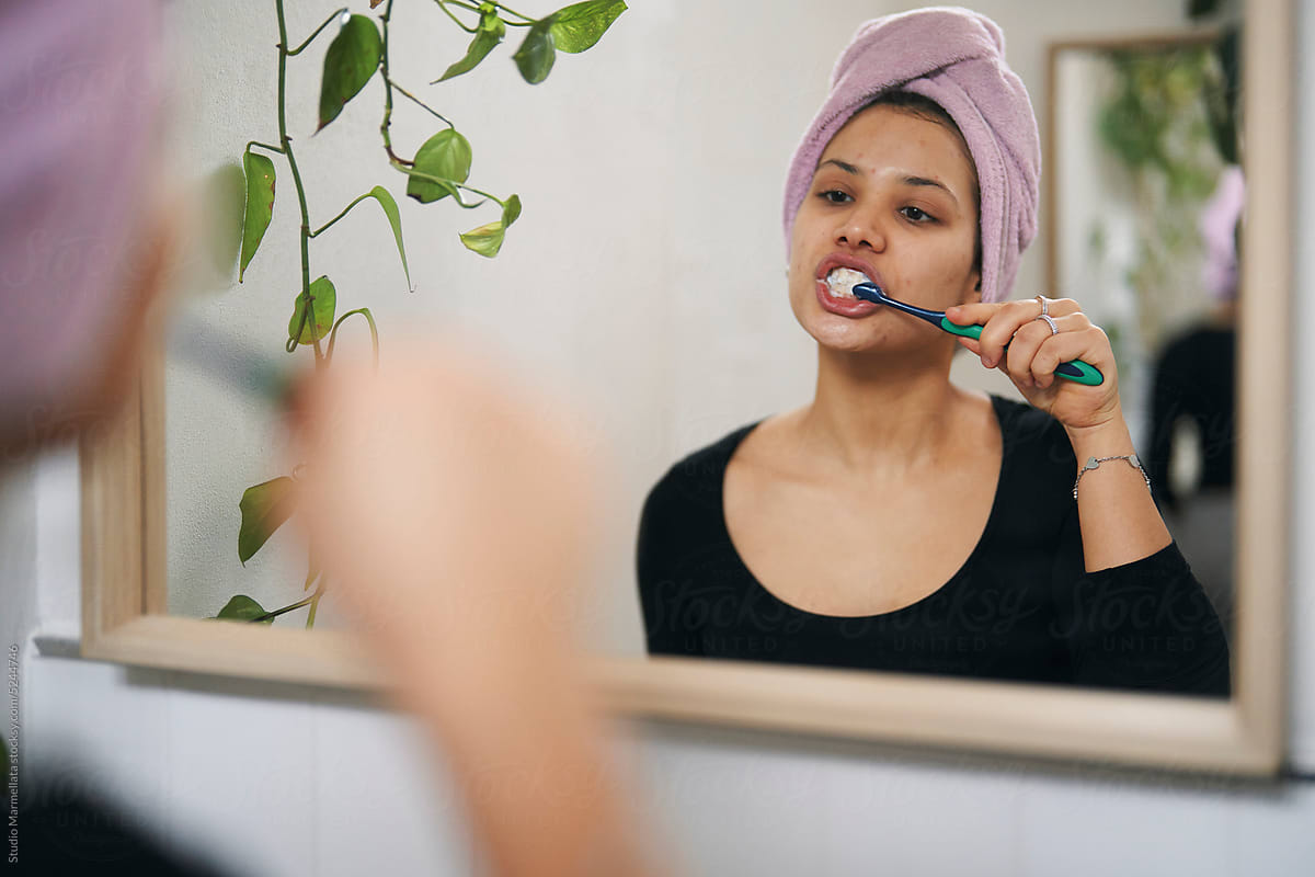 Young woman brushing teeth and looking in mirror