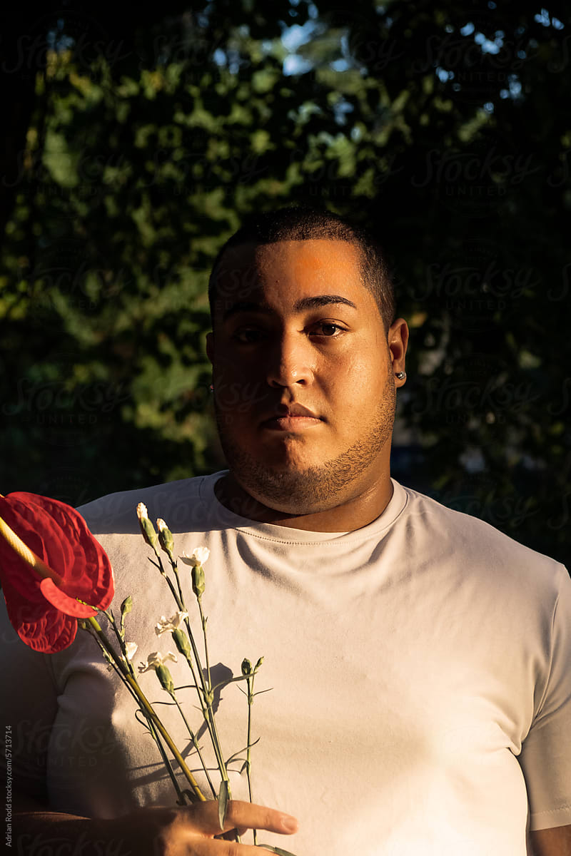 Portrait of plus size black boy with red and white flowers in hand.