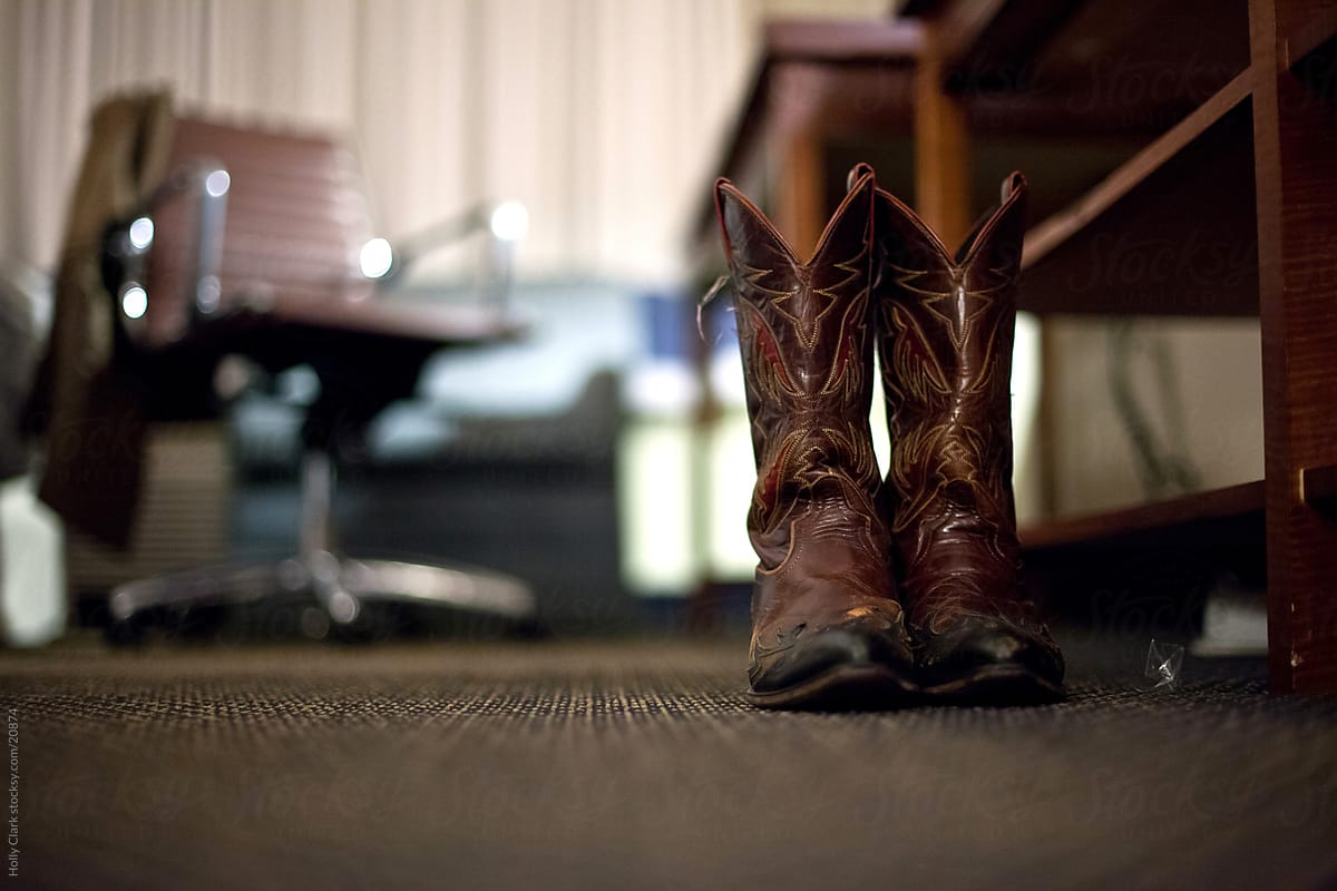 Well-worn cowboy boots sitting on hotel bedroom carpet
