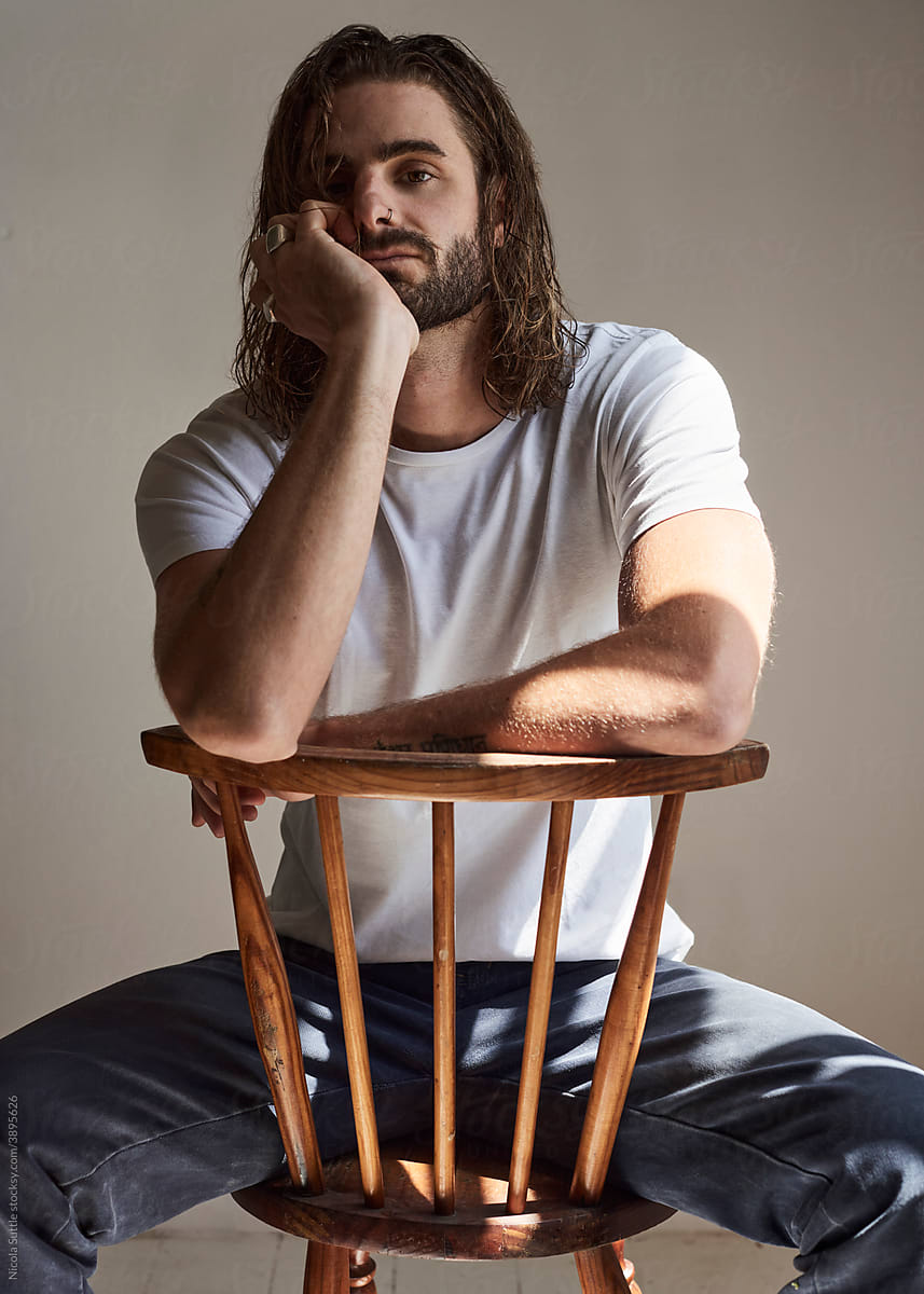 Pensive portrait of a young man straddling the back of a chair