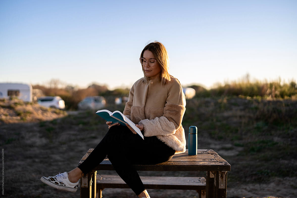 Serious woman reading book on bench in countryside