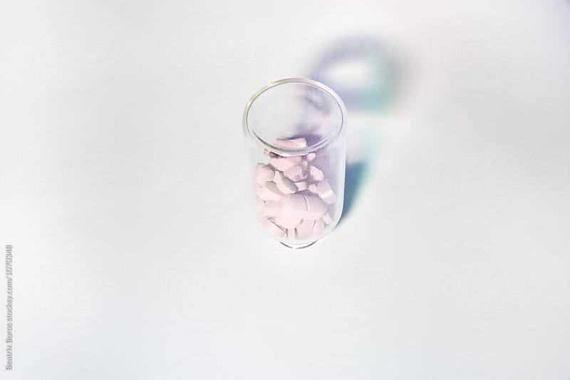 an upside down bottle full of pink medicines on white background